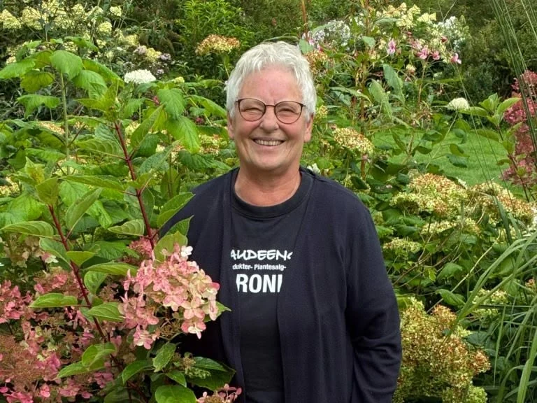 Hanne i sort Staudeengen-trøje i haven foran blomstrende hortensiaer.