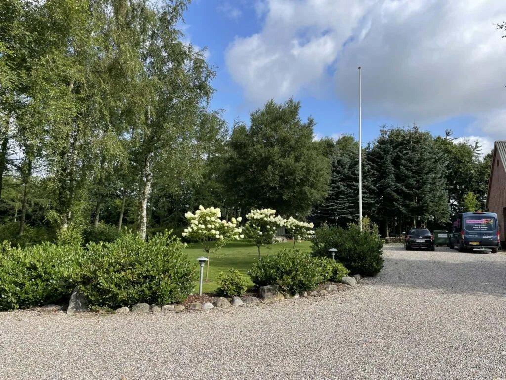 Ankomsten: gruspladsen med hortensiabed og hæk og biler parkeret i højre side.