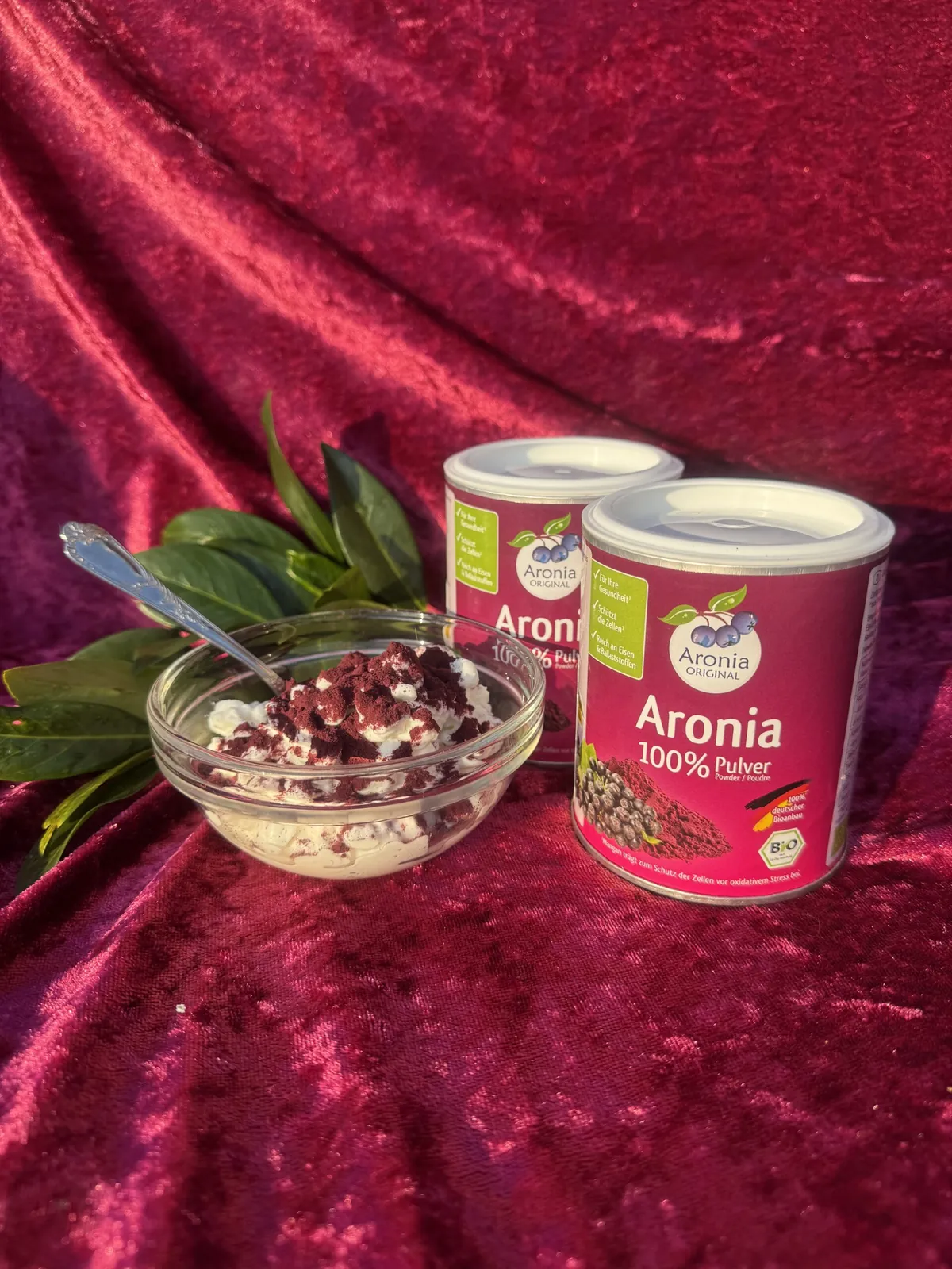 Aroniapulver rørt i en skål yoghurt ved siden af to dåser Aronia 100 % pulver.