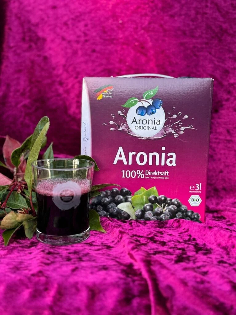 3-liters bag-in-box med aroniasaft, et fyldt glas saft og en gren med mørke aroniabær.