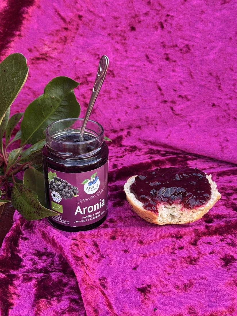 Åbent glas aroniasyltetøj med ske og en bolle smurt med syltetøj.